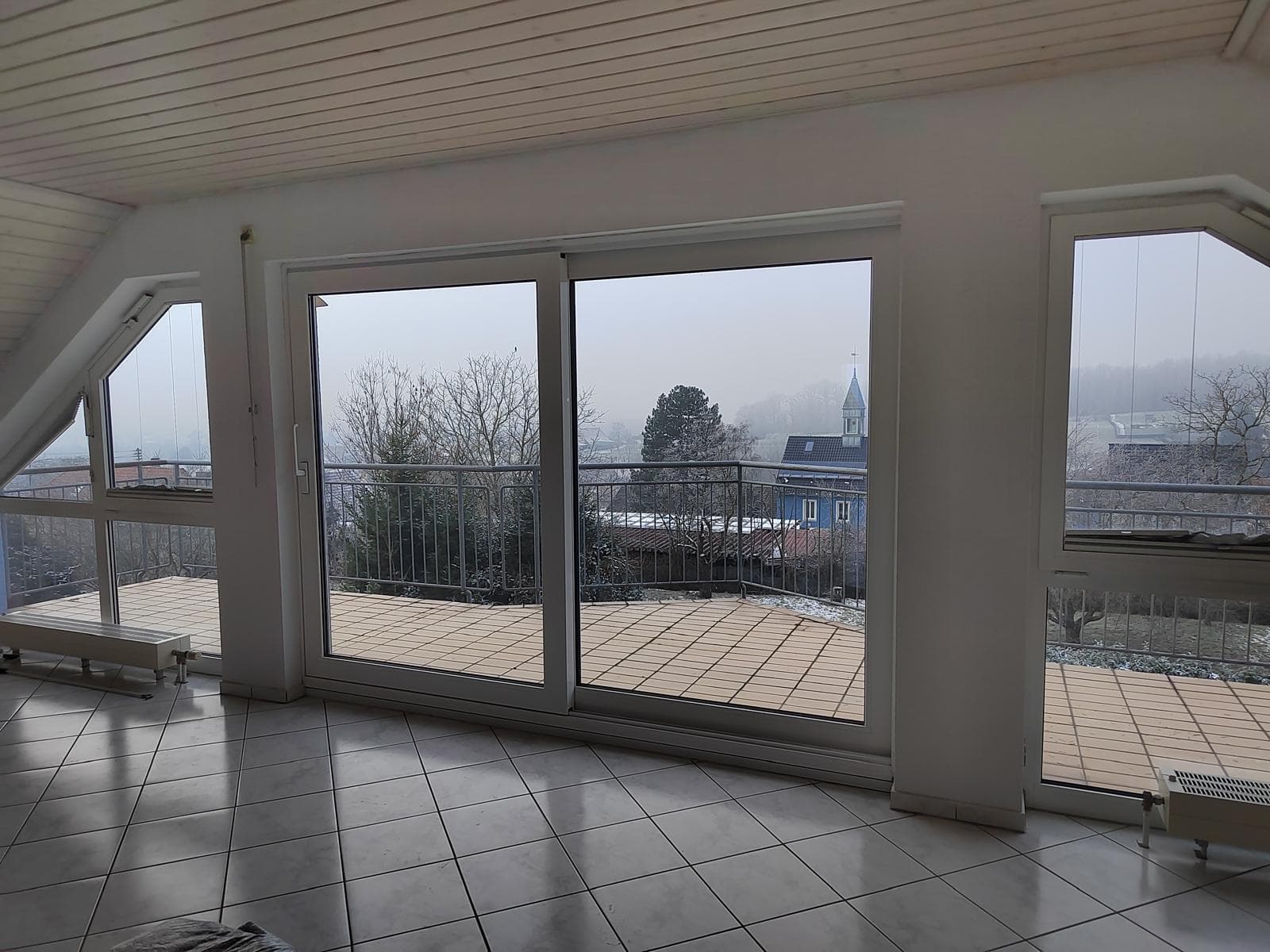 Blick durch die Schiebetür auf den Balkon, Ort und Kirchturm im Hintergrund